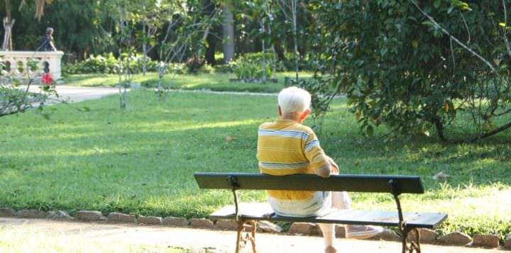 Vanhus istuu puistonpenkillä kesällä